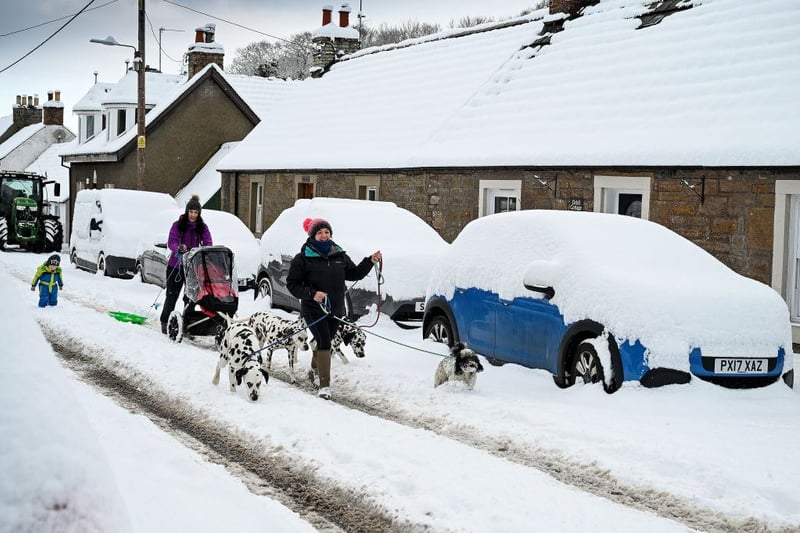 Members of the public can be seen taking their dogs for a walk in the deep snow in Dunning, Scotland.