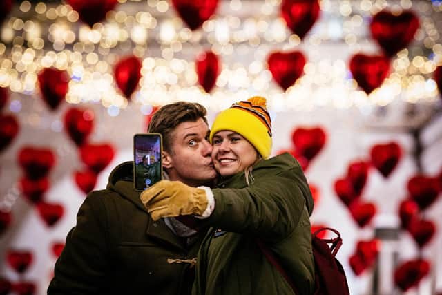 A couple kisses as they pose for a selfie under heart-shaped balloons displayed on the eve of Valentine's Day