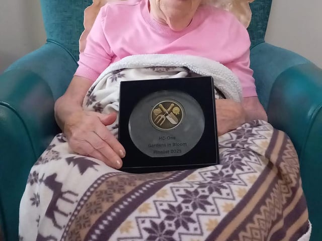 Resident at HC-One Scotland’s Highgate Care Home with their gardening plaque