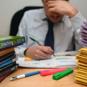 A school teacher looking stressed next to piles of classroom books.