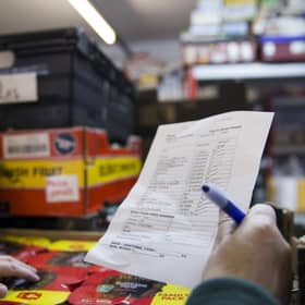 A volunteer with a packing list selecting items from it for the food parcel in the food bank warehouse