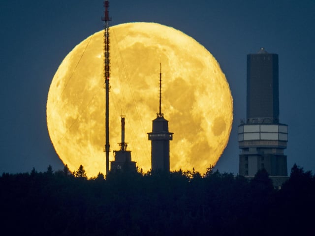 The full moon sets behind the telecommunication devices on top of the Feldberg mountain near Frankfurt, Germany, early Wednesday, June 15, 2022.In Frankfurt, it rose behind the German city’s banking district’s skyline.  (AP Photo/Michael Probst)