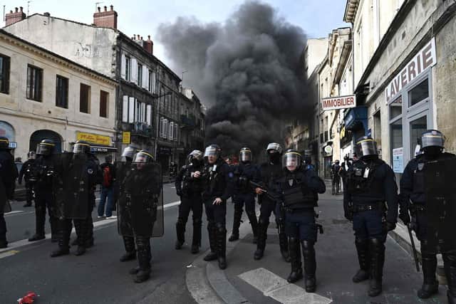 French French Republican Security Corps (CRS - Compagnies Republicaines de Securite) police officers in riot gear operate during a demonstration, with a smoke rising in the background, a week after the government pushed a pensions reform through parliament without a vote, using the article 49.3 of the constitution. (Photo by PHILIPPE LOPEZ/AFP via Getty Images)