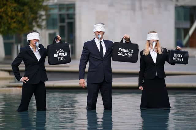 Suited performers from Ocean Rebellion, wearing blindfolds and gagged with dead fish, protest at Holyrood Pond, outside the Scottish Parliament in Edinburgh, calling on Scottish Government to wind down the environmental tragedy of salmon farming with a just transition for workers. Picture date: Friday October 7, 2022.