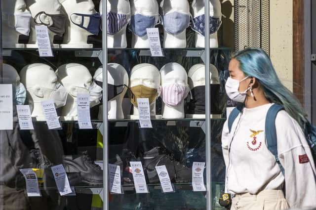 A woman wearing a protective face mask walks past a shop selling masks in Edinburgh city centre