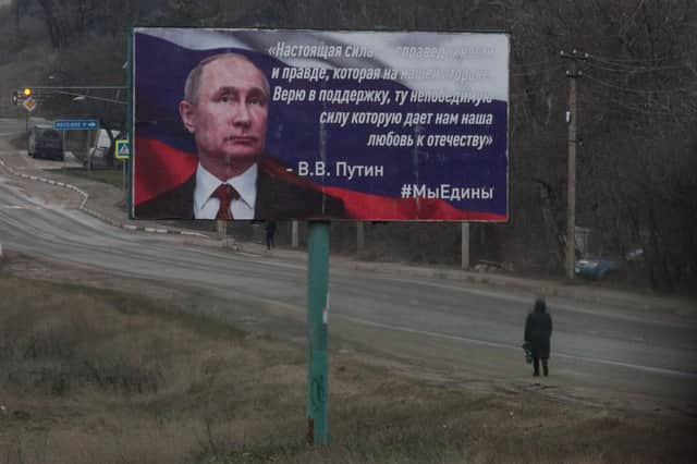 A woman walks past a billboard in Simferopol, Crimea, which quotes Vladimir Putin claiming truth is on Russia's side and hailing the 'invincible strength which our love for the Fatherland gives us' (Picture: stringer/AFP via Getty Images)