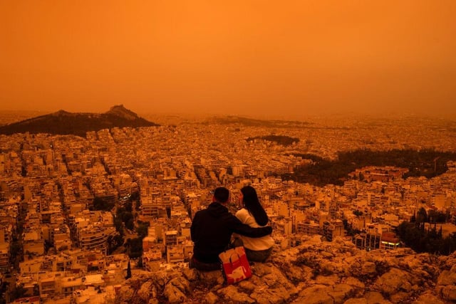 A couple sits on Tourkovounia hill, as southerly winds carry waves of Saharan dust, in Athens.