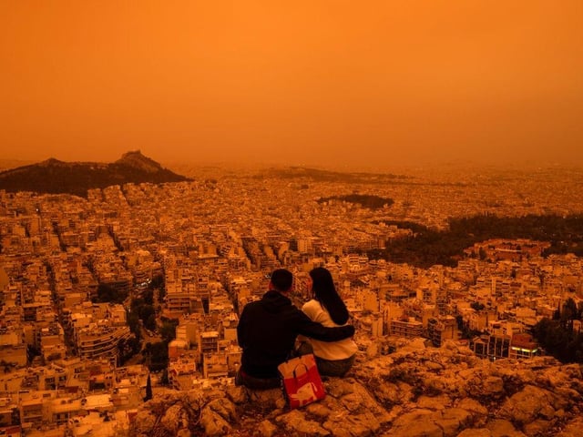 A couple sits on Tourkovounia hill, as southerly winds carry waves of Saharan dust, in Athens.