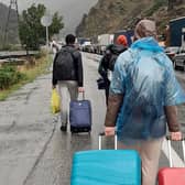 TOPSHOT - People carrying luggage walk past vehicles with Russian license plates on the Russian side of the border towards the Nizhniy Lars customs checkpoint between Georgia and Russia on Sunday. - Russian authorities acknowledged a "significant" influx of cars trying to cross from Russia into Georgia.