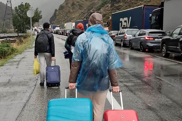 TOPSHOT - People carrying luggage walk past vehicles with Russian license plates on the Russian side of the border towards the Nizhniy Lars customs checkpoint between Georgia and Russia on Sunday. - Russian authorities acknowledged a "significant" influx of cars trying to cross from Russia into Georgia.