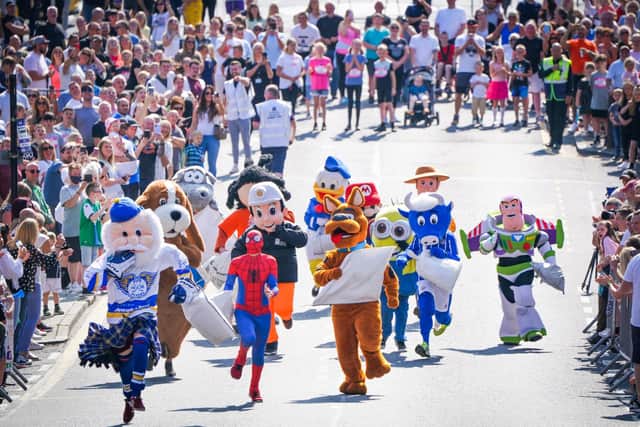 Competitors in the Mascot Race take part in the Scottish Coal Carrying Championships through the streets of Kelty in Fife.  Picture date: Saturday August 28, 2021. PA Photo. The annual event is one of only two Coal Races in the world and the men's race requires participants to carry a 50-kilo bag of coal and the women's race requires a 25-kilo bag of coal to be carried over 1000 metres through the village. Photo credit should read: Jane Barlow/PA Wire 