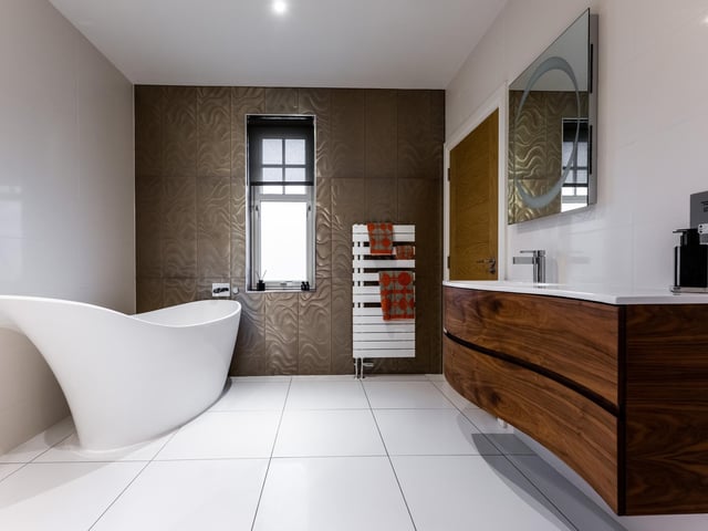 The sleek bathroom, by Laings of Inverurie, features glass tiling and a free-standing bath.