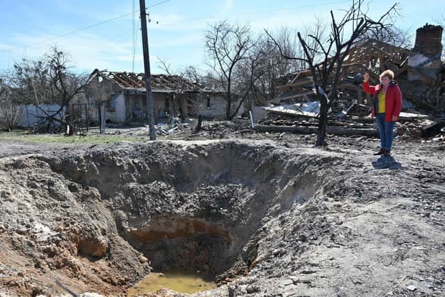 A woman gestures past a shell crater and destroyed houses in the outskirts of Ivankiv, Kyiv