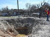 A woman gestures past a shell crater and destroyed houses in the outskirts of Ivankiv, Kyiv