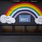 A man wearing a face mask walks past a rainbow graffiti in support of the NHS in Soho, central London