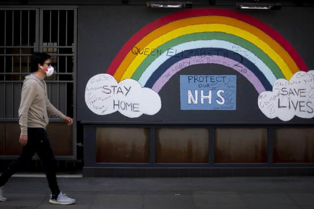 A man wearing a face mask walks past a rainbow graffiti in support of the NHS in Soho, central London