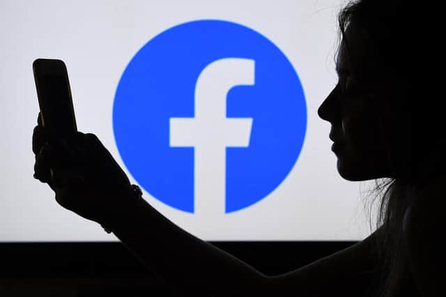 In this photo illustration, a person looks at a smart phone with a Facebook App logo displayed on the background, on August 17, 2021, in Arlington, Virginia. (Photo by OLIVIER DOULIERY / AFP) (Photo by OLIVIER DOULIERY/AFP via Getty Images)