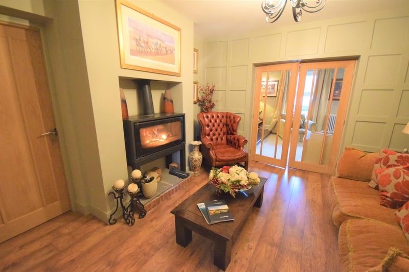 A really cosy room which has a multi fuel burner set on a stone hearth, panelled style walls, socket points, laminate flooring,