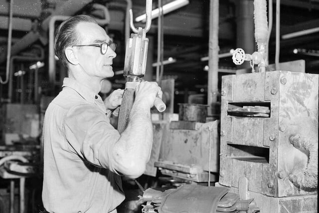A worker freeing the neck of a newly pressed hot water bottle on the production line in July 1958