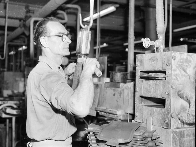 A worker freeing the neck of a newly pressed hot water bottle on the production line in July 1958