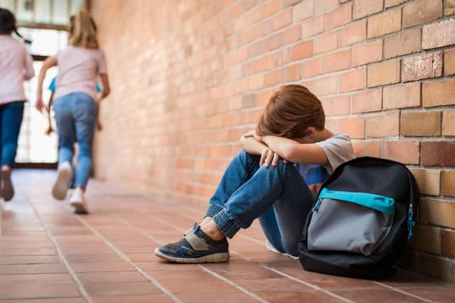 Schoolboy sitting on corridor with hands on knees and head between his legs.