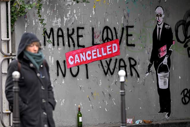 A woman walks past a street art depicting Russian president Vladimir Putin putting a "cancelled" poster over a "Make Love Not War" writting, in Paris. Picture: Emmanuel Dunand/AFP via Getty Images