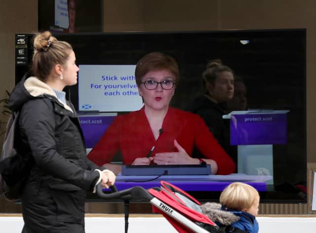 A member of the public walks past a TV screen at The Sound Counsel in Edinburgh as Nicola Sturgeon takes part in a virtual sitting of the Scottish Parliament (Picture: Andrew Milligan/PA Wire)