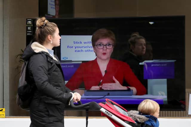 A member of the public walks past a TV screen at The Sound Counsel in Edinburgh as Nicola Sturgeon takes part in a virtual sitting of the Scottish Parliament (Picture: Andrew Milligan/PA Wire)