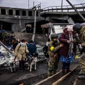 Ukrainian soldiers help an elderly woman to cross a destroyed bridge as she evacuates the city of Irpin, northwest of Kyiv, on March 7, 2022. (Photo by Dimitar DILKOFF / AFP) (Photo by DIMITAR DILKOFF/AFP via Getty Images)