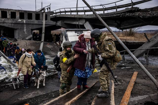 Ukrainian soldiers help an elderly woman to cross a destroyed bridge as she evacuates the city of Irpin, northwest of Kyiv, on March 7, 2022. (Photo by Dimitar DILKOFF / AFP) (Photo by DIMITAR DILKOFF/AFP via Getty Images)