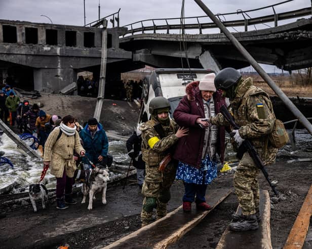Ukrainian soldiers help an elderly woman to cross a destroyed bridge as she evacuates the city of Irpin, northwest of Kyiv, on March 7, 2022. (Photo by Dimitar DILKOFF / AFP) (Photo by DIMITAR DILKOFF/AFP via Getty Images)