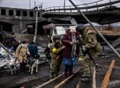 Ukrainian soldiers help an elderly woman to cross a destroyed bridge as she evacuates the city of Irpin, northwest of Kyiv, on March 7, 2022. (Photo by Dimitar DILKOFF / AFP) (Photo by DIMITAR DILKOFF/AFP via Getty Images)