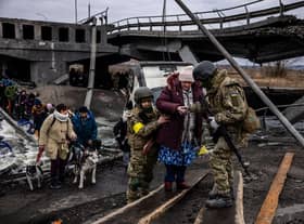 Ukrainian soldiers help an elderly woman to cross a destroyed bridge as she evacuates the city of Irpin, northwest of Kyiv, on March 7, 2022. (Photo by Dimitar DILKOFF / AFP) (Photo by DIMITAR DILKOFF/AFP via Getty Images)