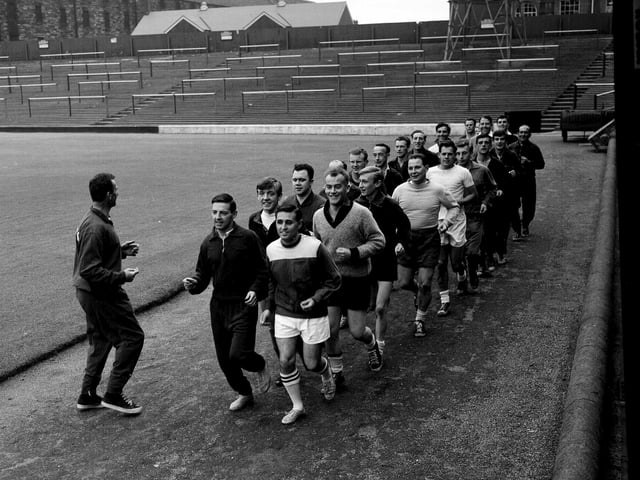 A group of referees join Hearts players for their pre-season training, with the Tynecastle terracing in the background, in August 1965.