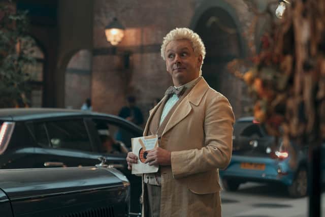 Aziraphale holding the Buddy Holly record Everyday, with a label on it which reads: The Resurrectionist, 66 Goat Gate, Edinburgh.