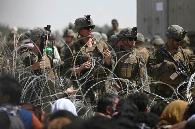 US soldiers stand guard behind barbed wire as Afghans hoping to flee the country sit on a roadside near Kabul Airport (Picture: Wakil Kohsar/AFP via Getty Images)