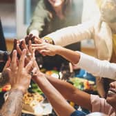 Group of people joining hands sitting at dinner table Pic: Adobe