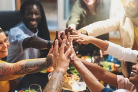Group of people joining hands sitting at dinner table Pic: Adobe