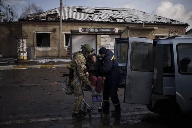 A Ukrainian soldier helps an elderly woman who was being evacuated on a shopping cart from Irpin, in the outskirts of Kyiv