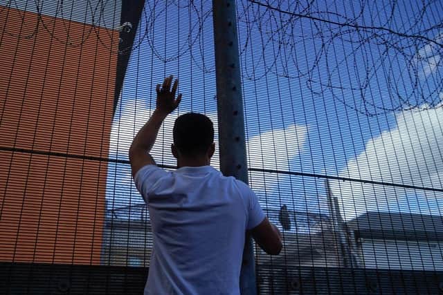 A protester communicates with those inside at the perimeter fence of Brook House immigration removal centre beside Gatwick Airport as demonstrators gather to protest against the UK government's intention to deport asylum-seekers to Rwanda.