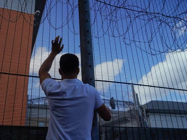 A protester communicates with those inside at the perimeter fence of Brook House immigration removal centre beside Gatwick Airport as demonstrators gather to protest against the UK government's intention to deport asylum-seekers to Rwanda.