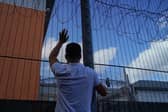 A protester communicates with those inside at the perimeter fence of Brook House immigration removal centre beside Gatwick Airport as demonstrators gather to protest against the UK government's intention to deport asylum-seekers to Rwanda.
