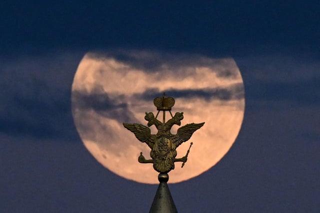 The full moon is pictured behind the two-headed eagle, the national symbol of Russia atop a building on Red Square in Moscow (Photo by KIRILL KUDRYAVTSEV/AFP via Getty Images)