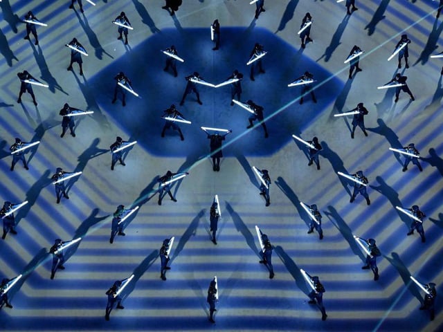 Performers dance with bars of light during the ceremony.