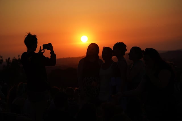 A festivalgoer takes a photo of the sunset from above the site of the Glastonbury Festival at Worthy Farm in Somerset.