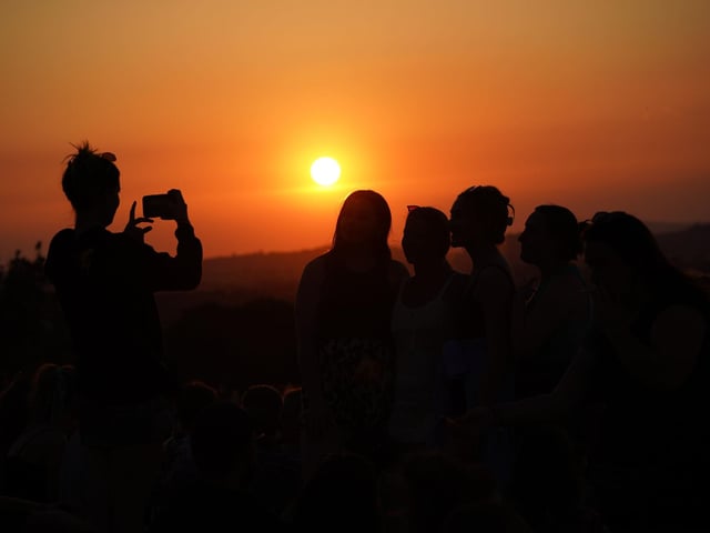 A festivalgoer takes a photo of the sunset from above the site of the Glastonbury Festival at Worthy Farm in Somerset.