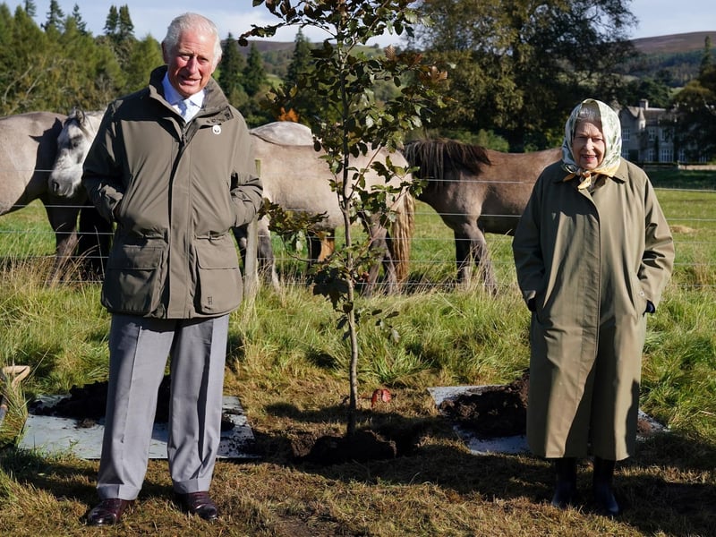 Queen Elizabeth II and Prince Charles pose alongside the tree which they planted to mark the start of the official planting season for the Queen's Green Canopy at the Balmoral Cricket Pavilion on October 1, 2021.