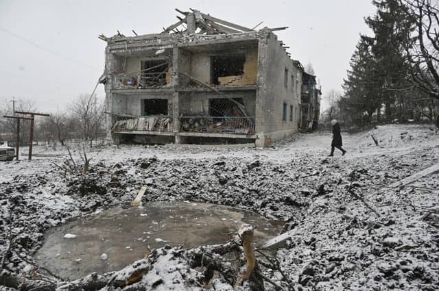 A local resident walks past a crater and a damaged residential building following a recent aerial bombardment in Kupiansk, Kharkiv region.