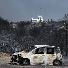 TOPSHOT - A burnt car in a charred area after a fire near the village of Kiotari, on the Greek island of Rhodes. Tens of thousands of people have already fled blazes on the island of Rhodes, with many frightened tourists scrambling to get home.