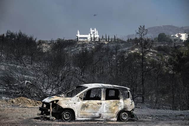 TOPSHOT - A burnt car in a charred area after a fire near the village of Kiotari, on the Greek island of Rhodes. Tens of thousands of people have already fled blazes on the island of Rhodes, with many frightened tourists scrambling to get home.